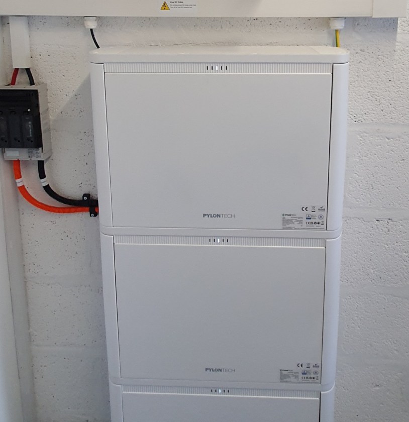 Three stacked Pylontech battery units mounted on a wall, connected to electrical components with visible wiring.